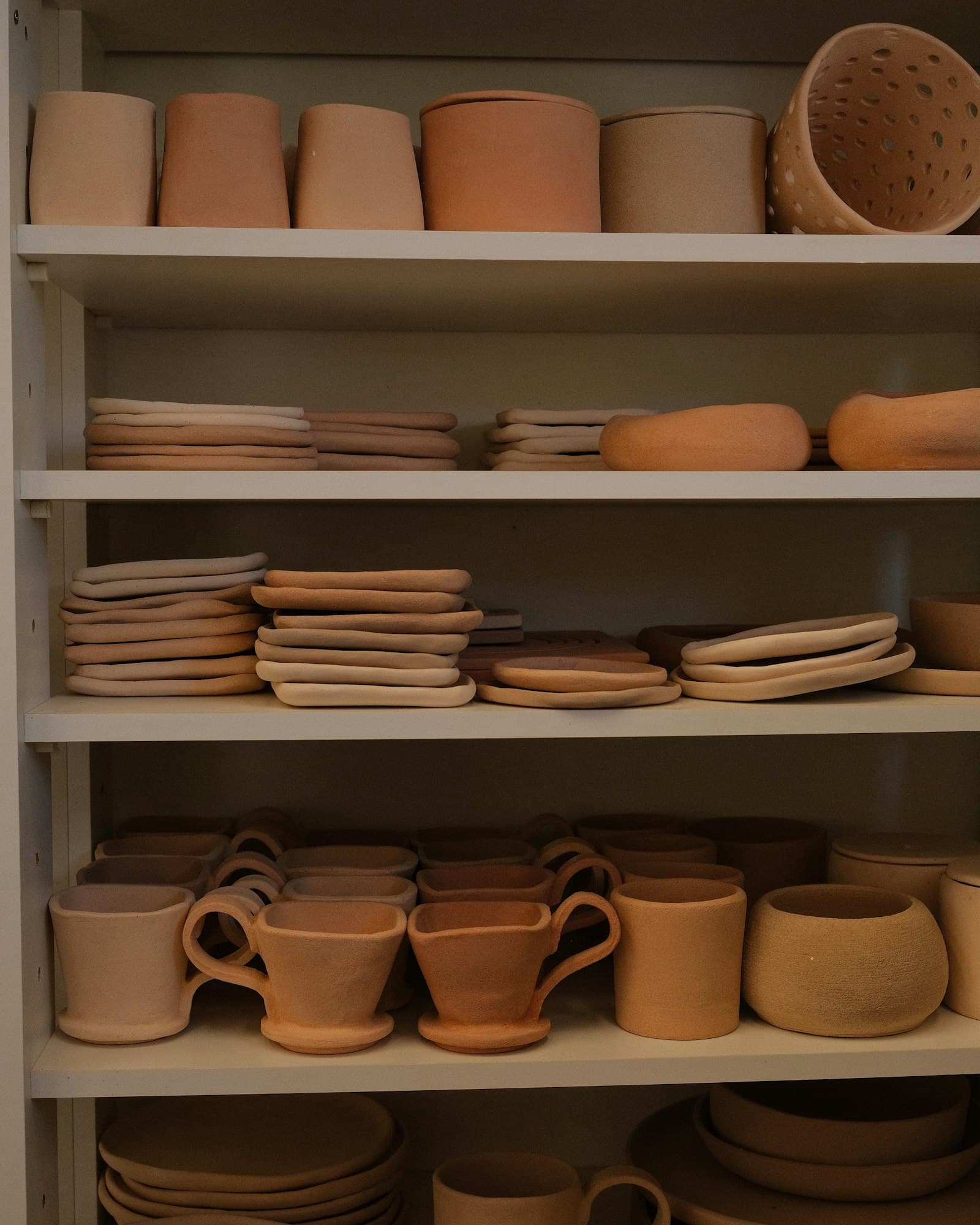 Estantes del taller con tazas, platos y cuencos de barro esperando el horno